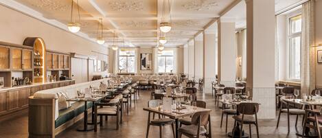 Un restaurante espacioso con techos altos, candelabros y una larga barra con asientos.