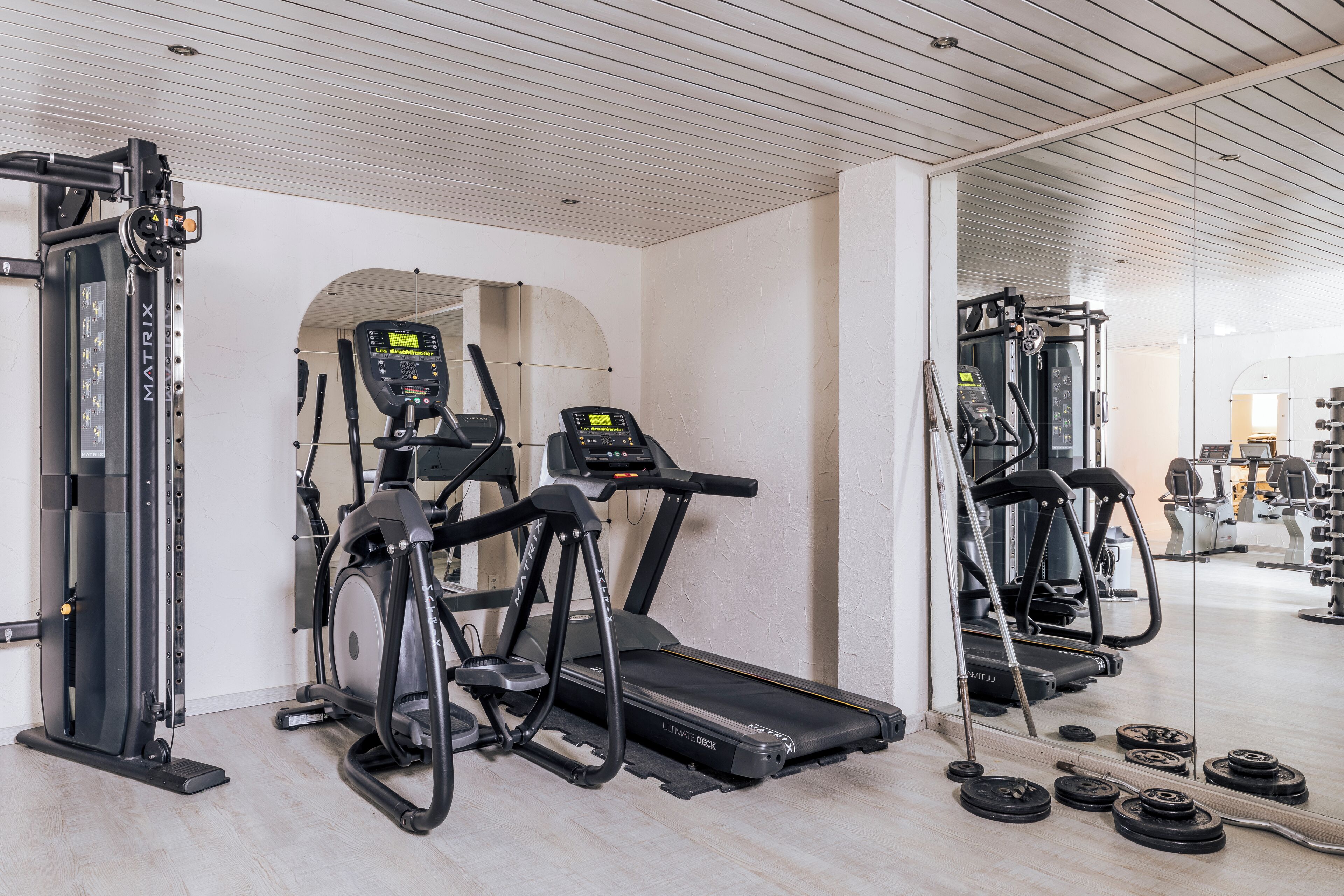 Een sportschool met loopbanden, een crosstrainer en een gewichtbank.