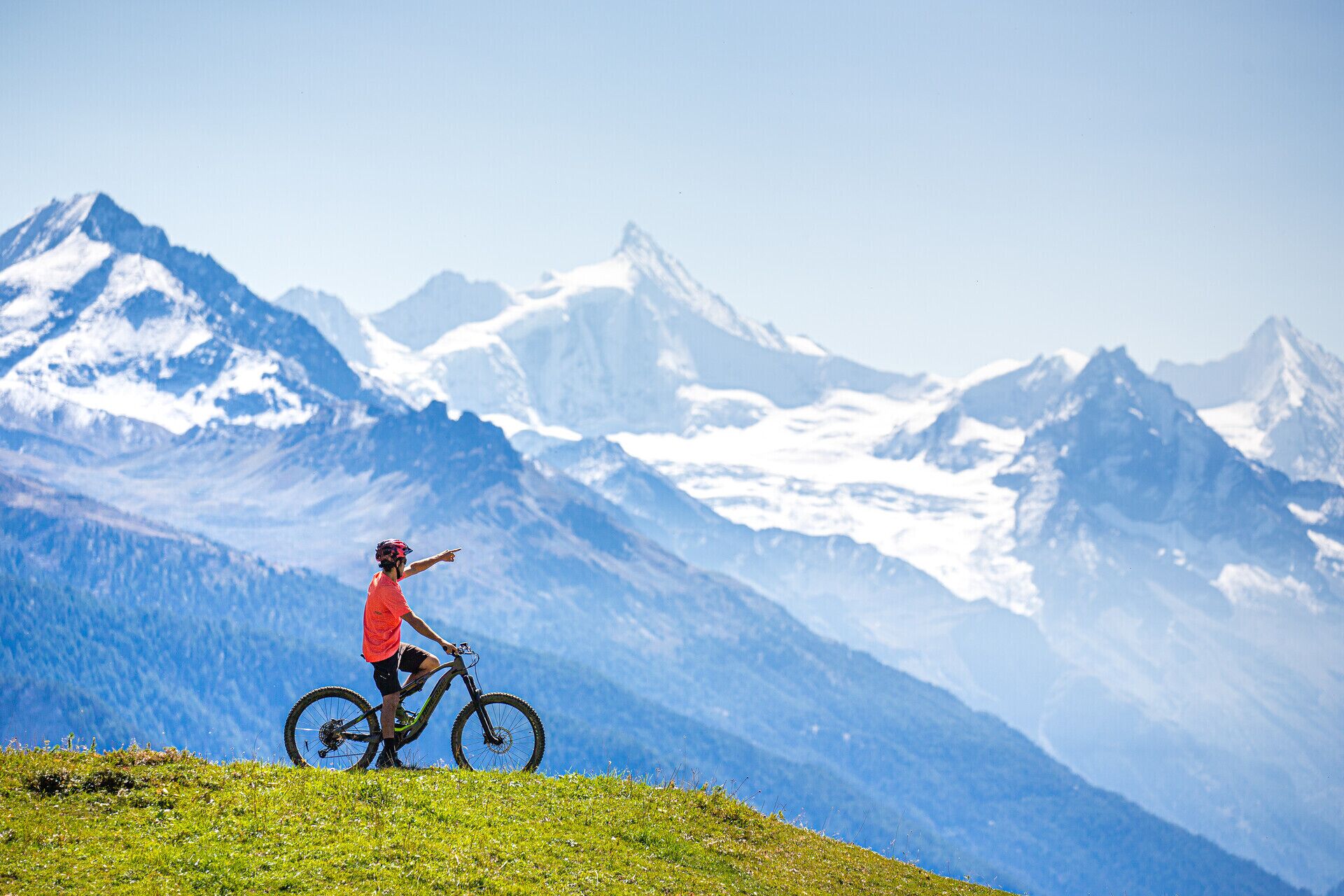 Una persona en bicicleta de montaña con vistas despejadas a montañas nevadas al fondo.
