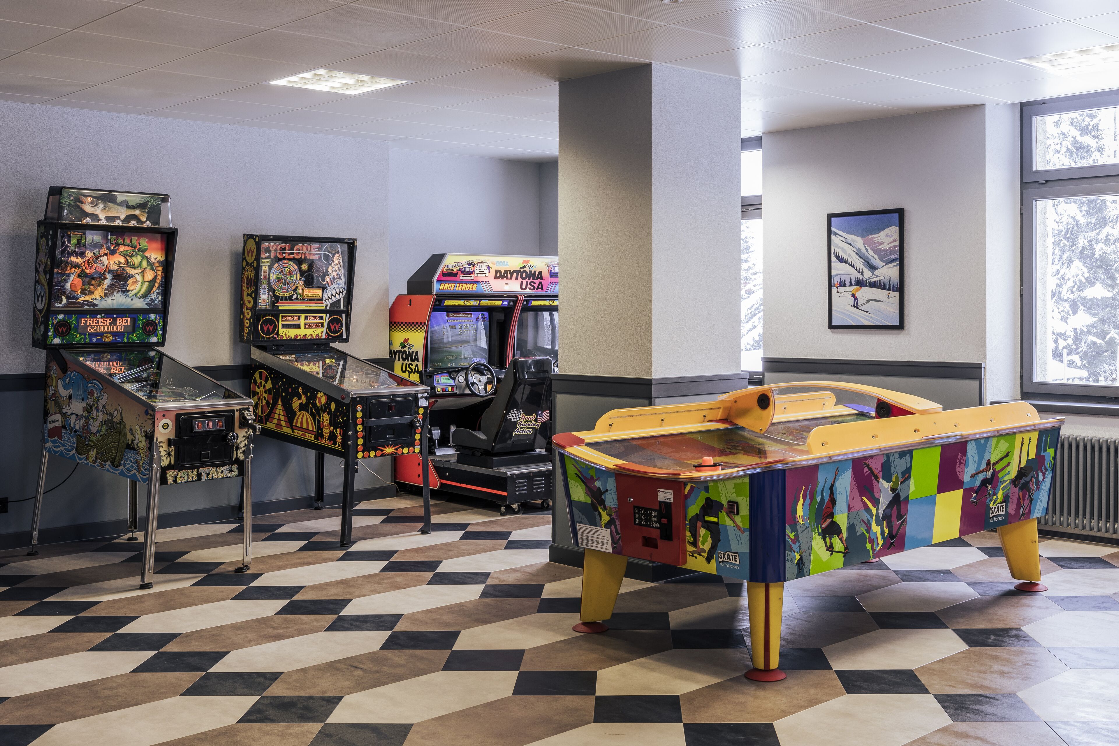 A room with arcade games, a checkered floor, and a window with a view of trees.