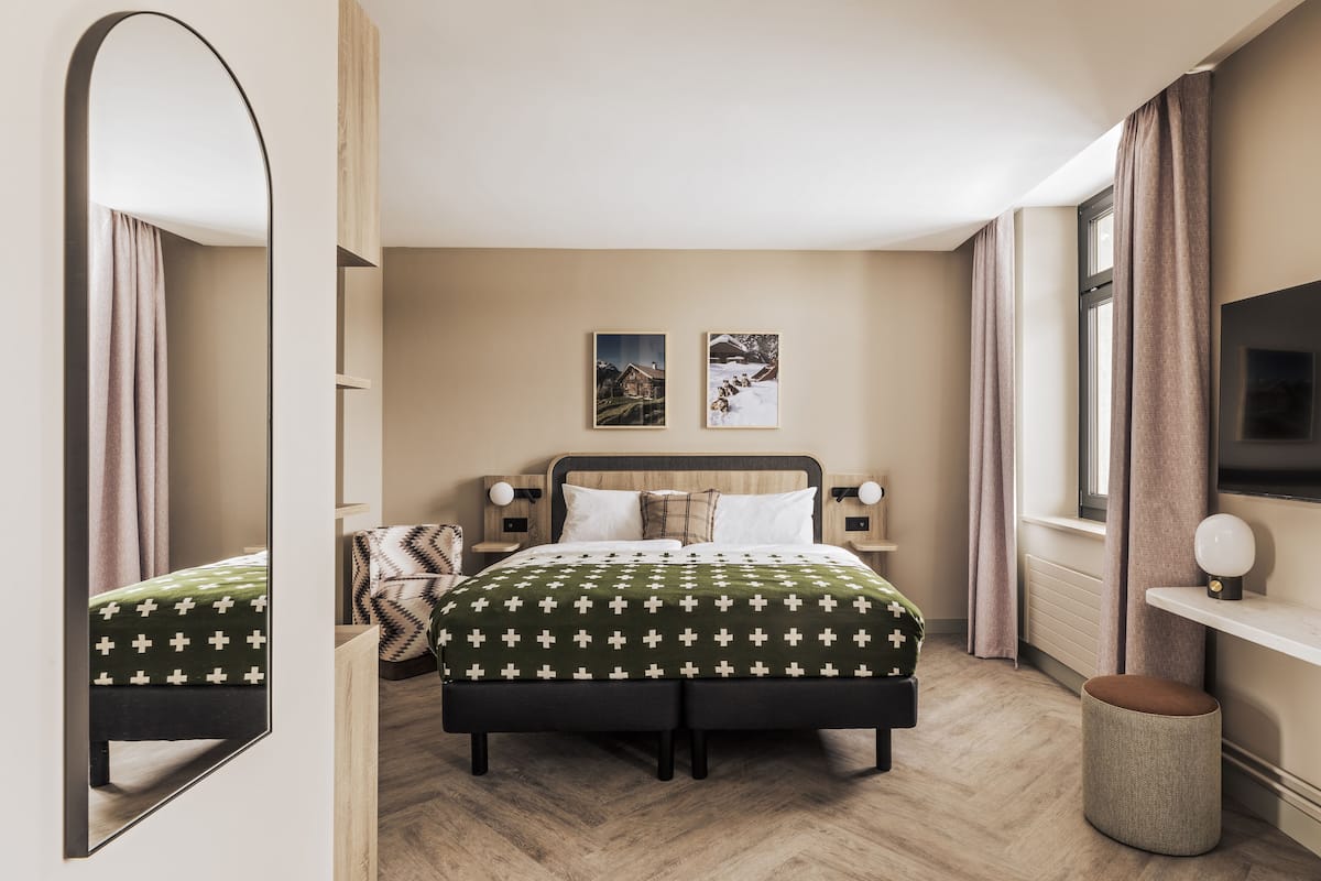 A modern hotel room with a large bed, a mirror, a television, and two framed pictures on the wall.