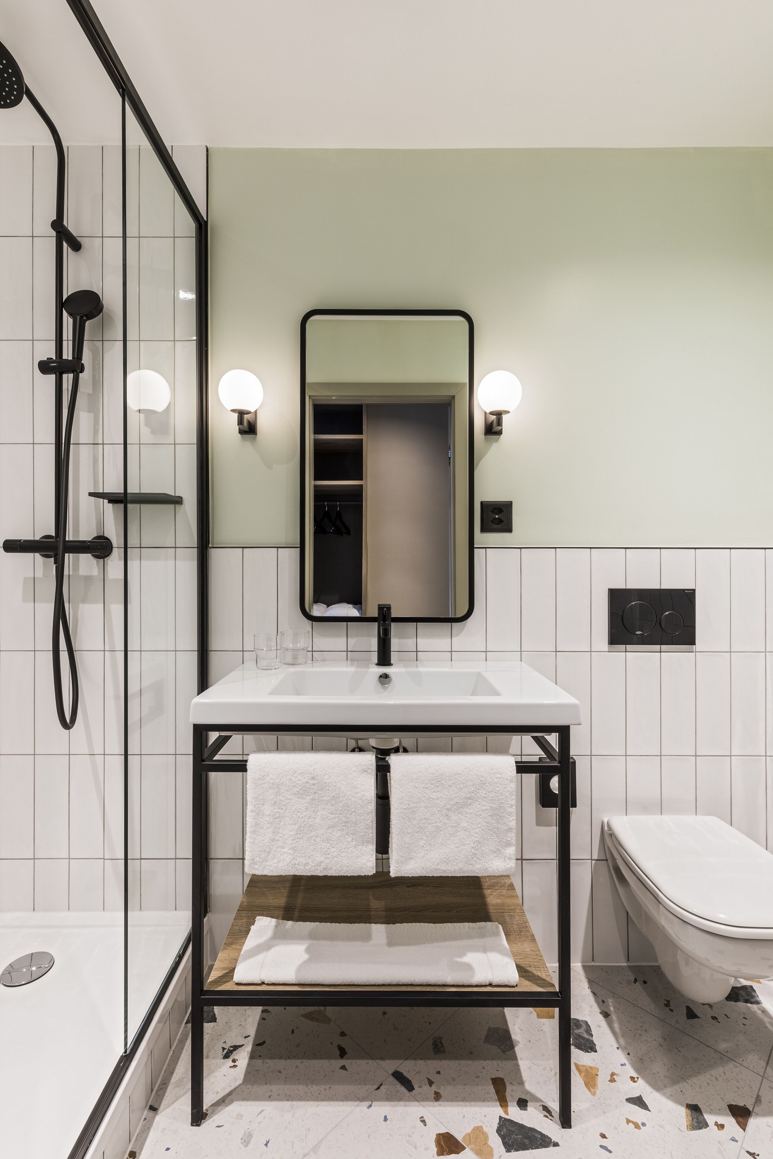 Ein modernes Badezimmer mit einer gläsernen Dusche, einem weißen Waschbecken mit Holzablage, einem Spiegel mit Wandleuchten und einer weißen Toilette.
