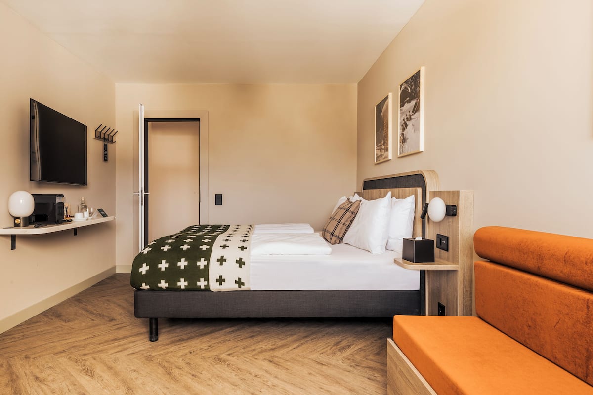 A modern hotel room with a bed, bedside tables, a TV, and a sofa.