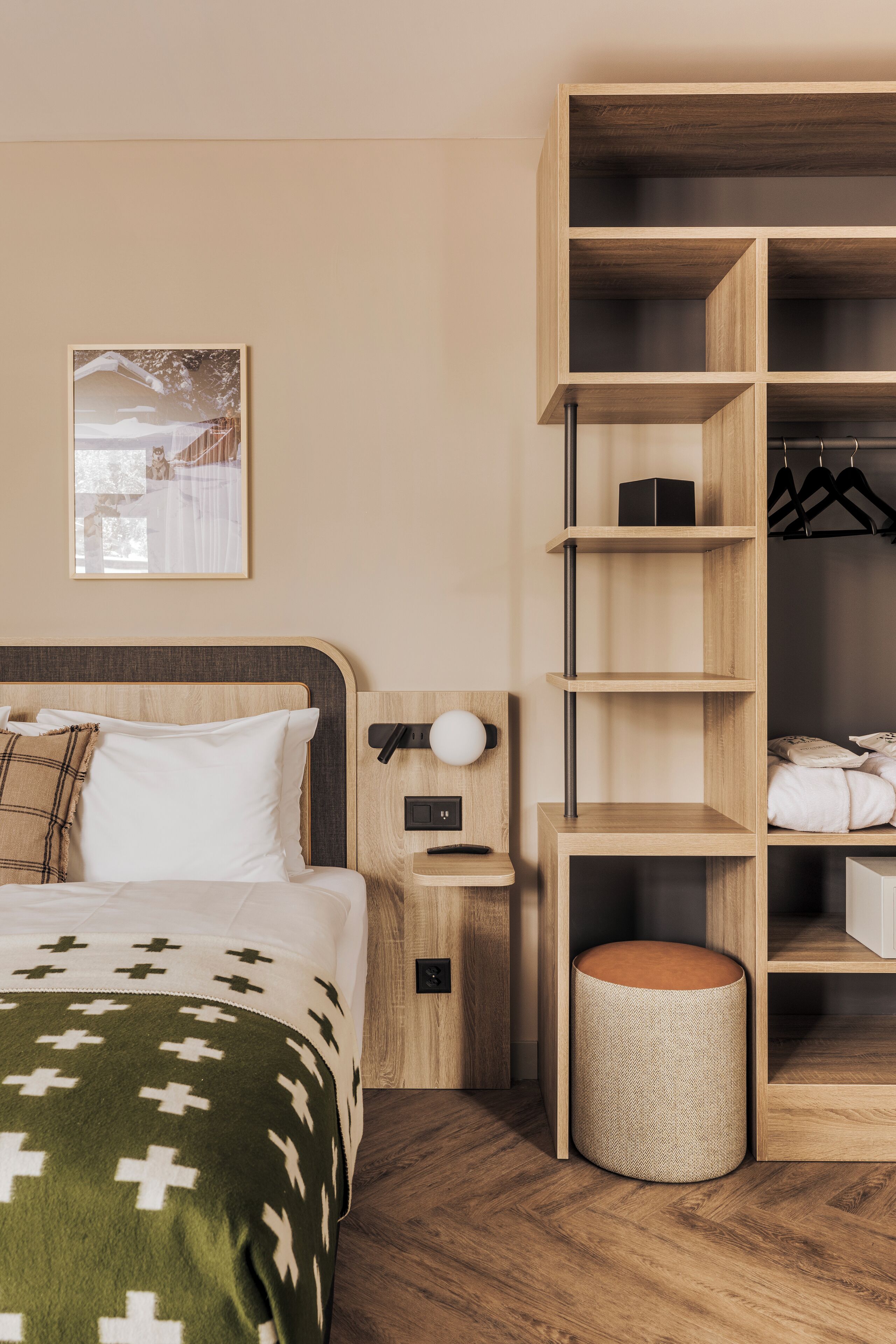 A neatly arranged hotel room with a bed, bedside table, lamp, and a built-in wardrobe with shelves.