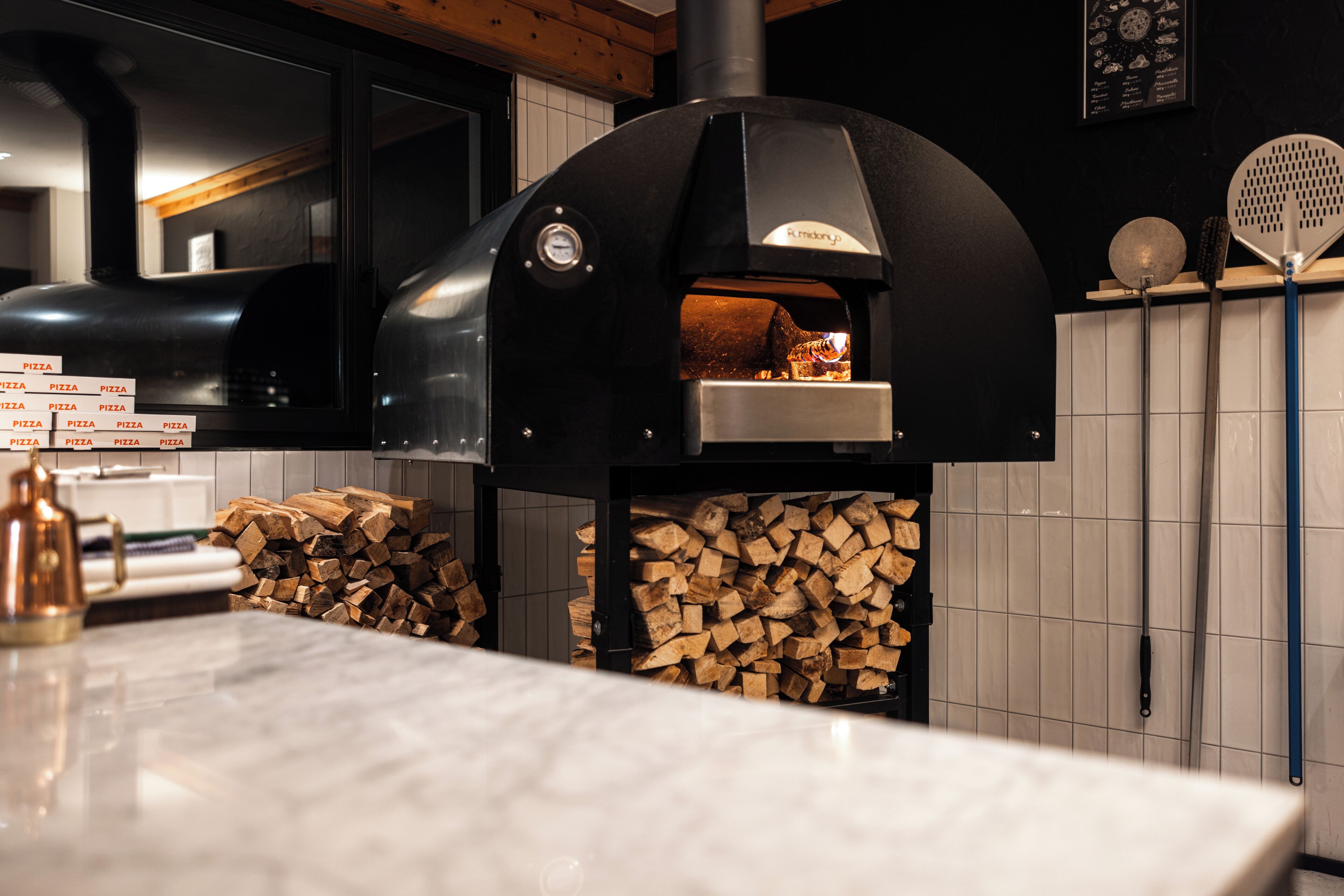 A kitchen with a wood-fired pizza oven, a marble countertop, and a stack of firewood.