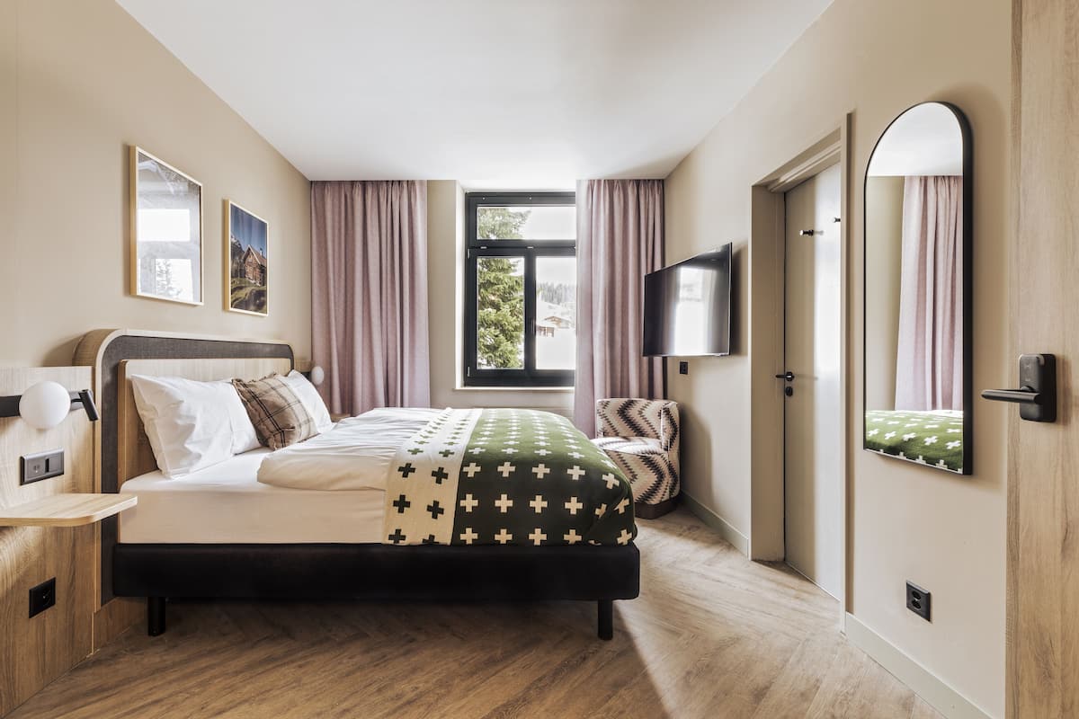 A modern bedroom with a bed, a TV, a window with curtains, and a door.