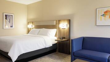 Ein Hotelzimmer mit Bett, Nachttisch mit Lampe, blauem Sofa und Holz-Couchtisch.