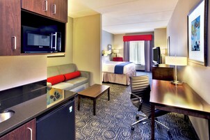 Una habitación de hotel con kitchenette, un sofá con cojines rojos, una cama con cubrecama azul, un escritorio con silla y un televisor.