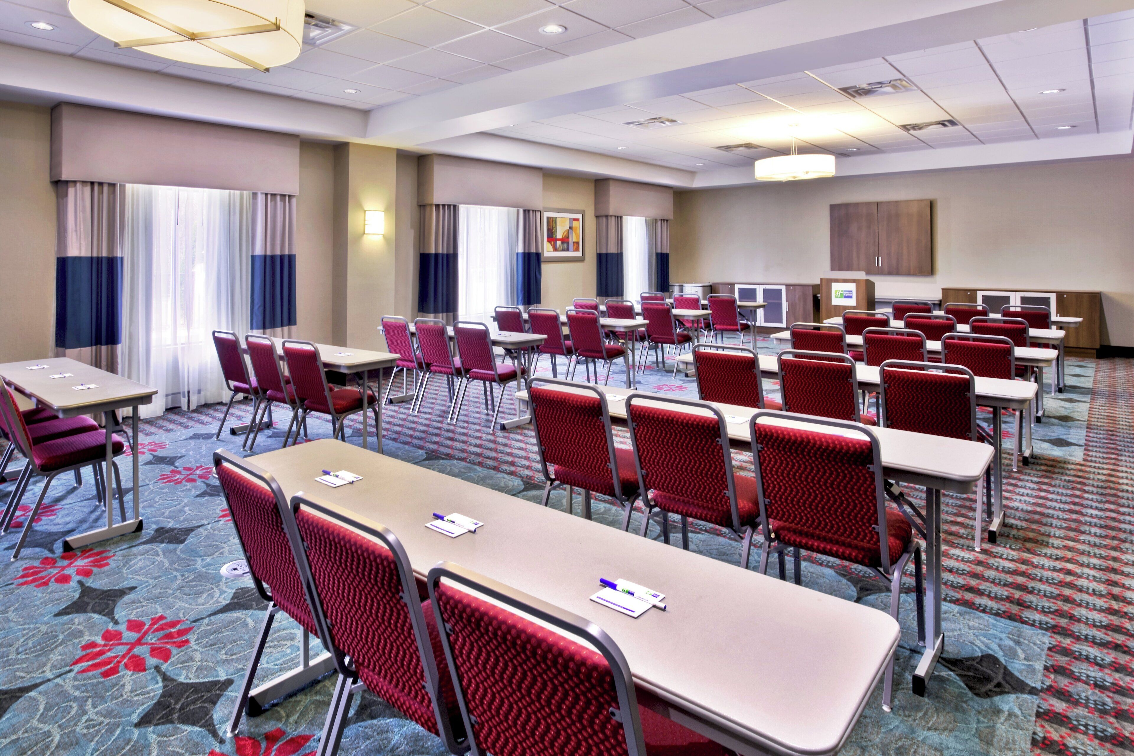 Une salle de conférence dotée de plusieurs tables et chaises, d’un sol recouvert de moquette et d’un plafond pourvu d’un éclairage encastré.