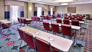 Un salón de conferencias con varias mesas y sillas, suelo alfombrado e iluminación empotrada en el techo.