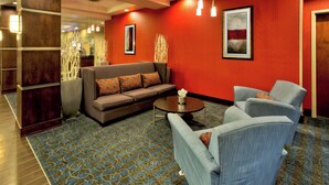Un vestíbulo de hotel con una pared roja, un sofá marrón, un sillón azul y una mesa de centro.