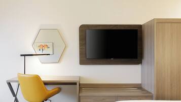 Una habitación de hotel con una cama, un escritorio con una silla, un televisor montado en la pared y un armario.