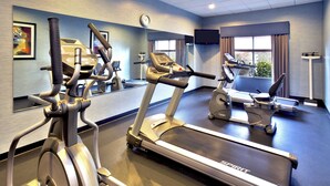 A gym with multiple exercise machines, a large mirror, and a clock on the wall.