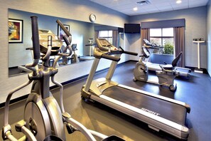 A gym with multiple exercise machines, a large mirror, and a clock on the wall.