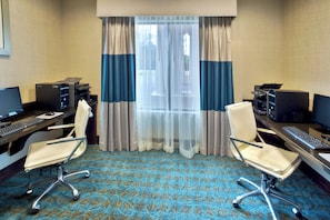 A hotel room with two desks, each with a computer and keyboard, a chair, and a large window with sheer curtains.