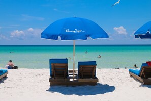 A beach with two blue umbrellas labeled "Pawny Jack," wooden lounge chairs, and a clear view of the ocean. - Bikini Beach Resort (Panama City Beach)