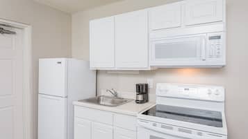 Una cocina con gabinetes blancos, un lavamanos de acero inoxidable, una cafetera y una estufa blanca.