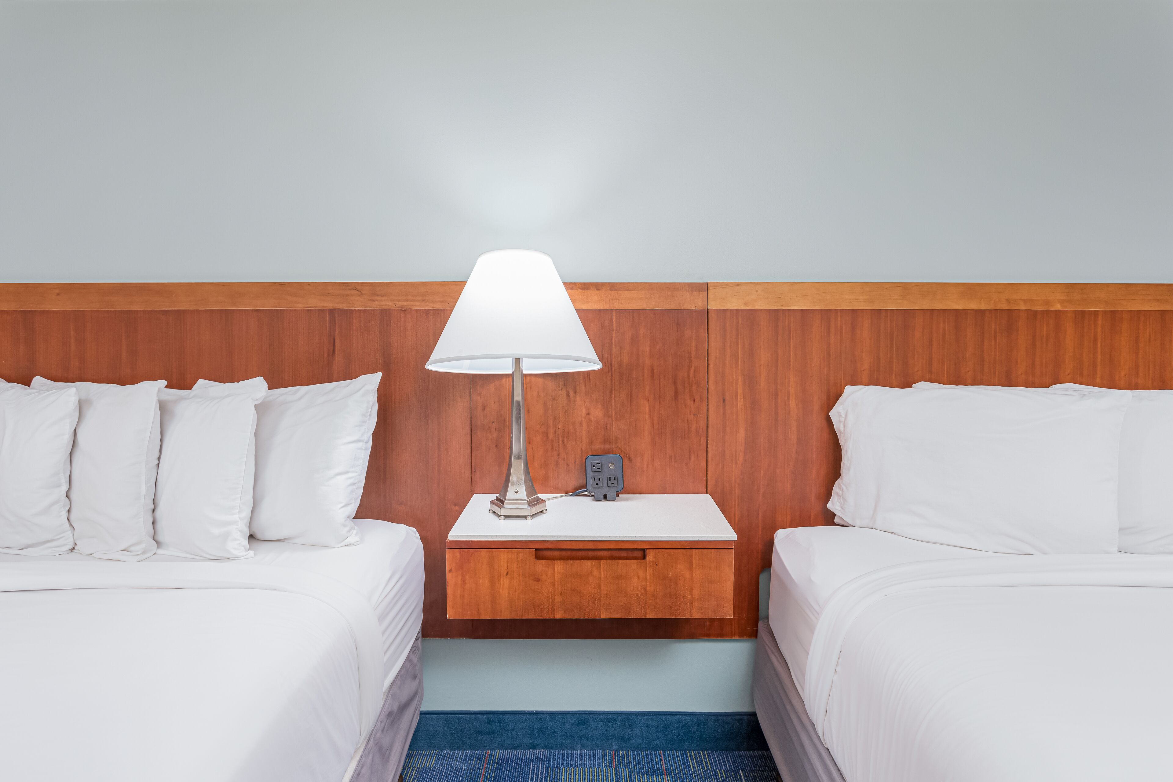 Une chambre d’hôtel avec deux lits, une table de chevet avec une lampe et une tête de lit en bois.