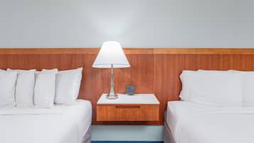 Una habitación de hotel con dos camas, una mesita de noche con lámpara y un cabecero de madera.