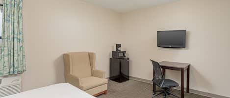 Een hotelkamer met een bed, een bureau, een stoel, een televisie en een kleine koelkast.