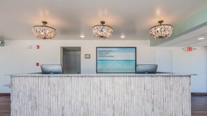 Een receptiebalie met een witte houtafwerking, drie kroonluchters, een digitaal scherm met informatie over de kamers en een vluchtwegbord.