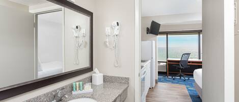 A hotel bathroom with a granite countertop sink, a large mirror, a hairdryer, and a telephone.