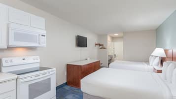 A hotel room with a kitchenette, a TV, a wooden dresser, two beds, and a lamp.