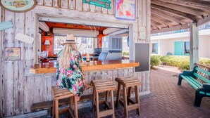 Een houten tiki bar met een toonbank, krukken en een bordje met de tekst 'TIKI BAR'.