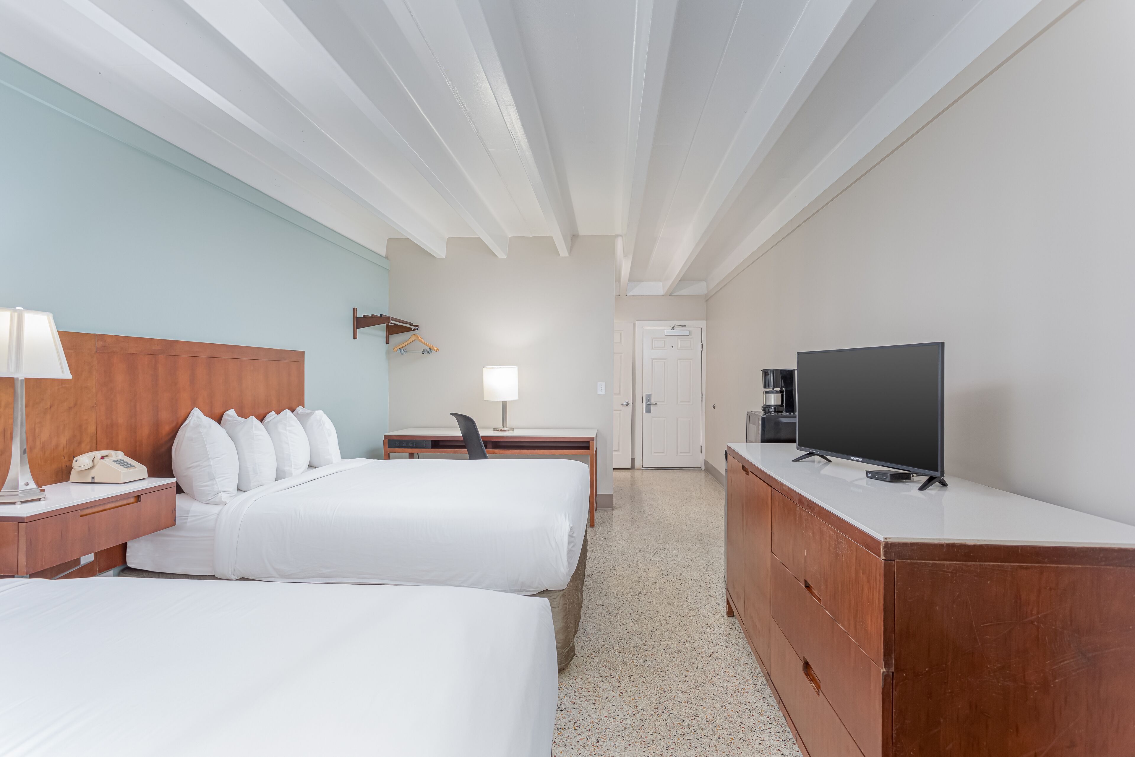 Una habitación de hotel con dos camas, un escritorio con silla, un televisor y un aparador.