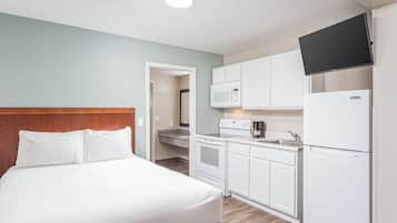 A compact hotel room with a bed, kitchenette, and a TV mounted on the wall.