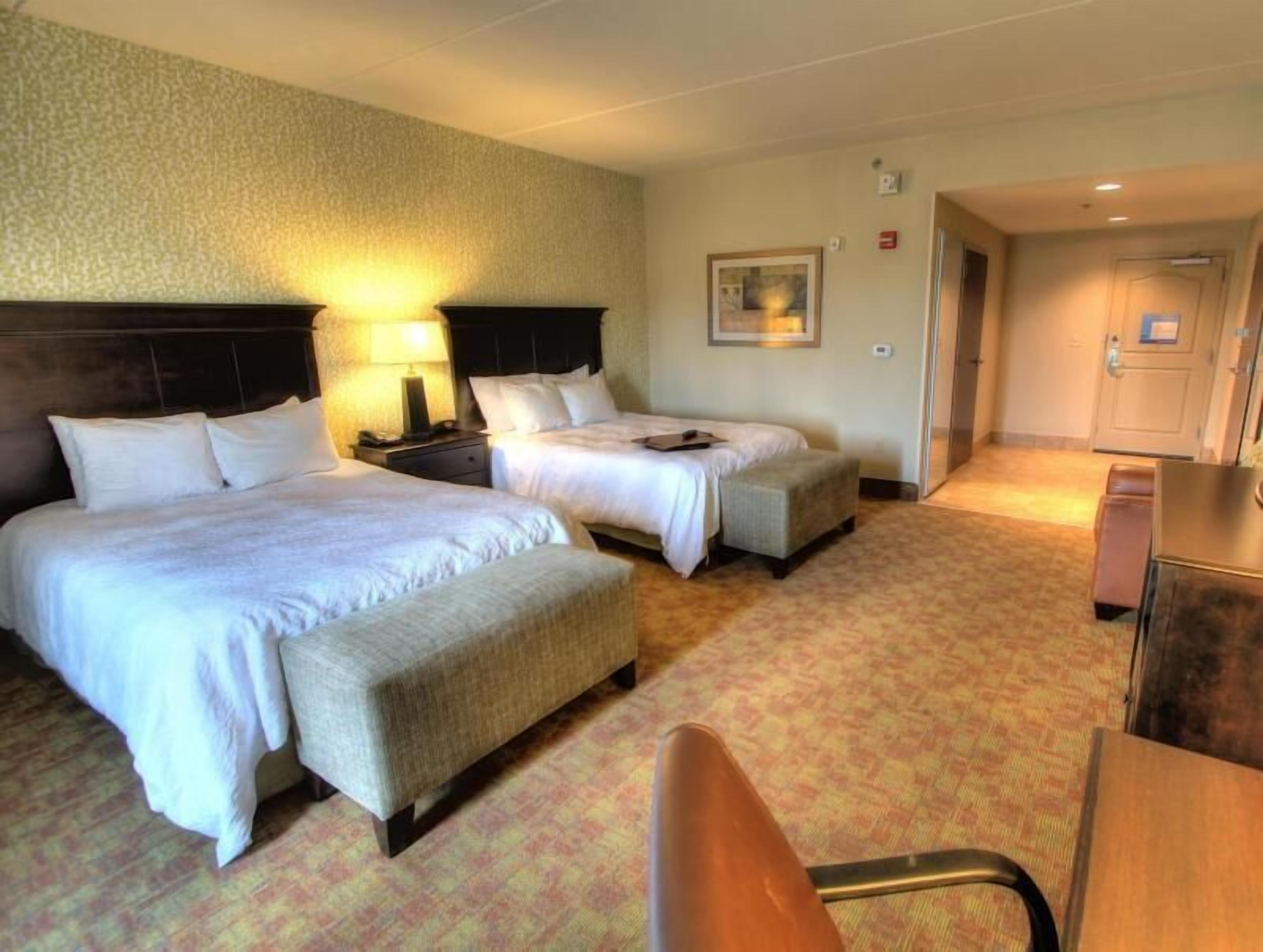 A hotel room with two beds, a desk, a chair, and a carpeted floor.