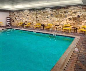 An indoor swimming pool with a stone wall backdrop and yellow chairs. - Hampton Inn Pigeon Forge (Pigeon Forge)