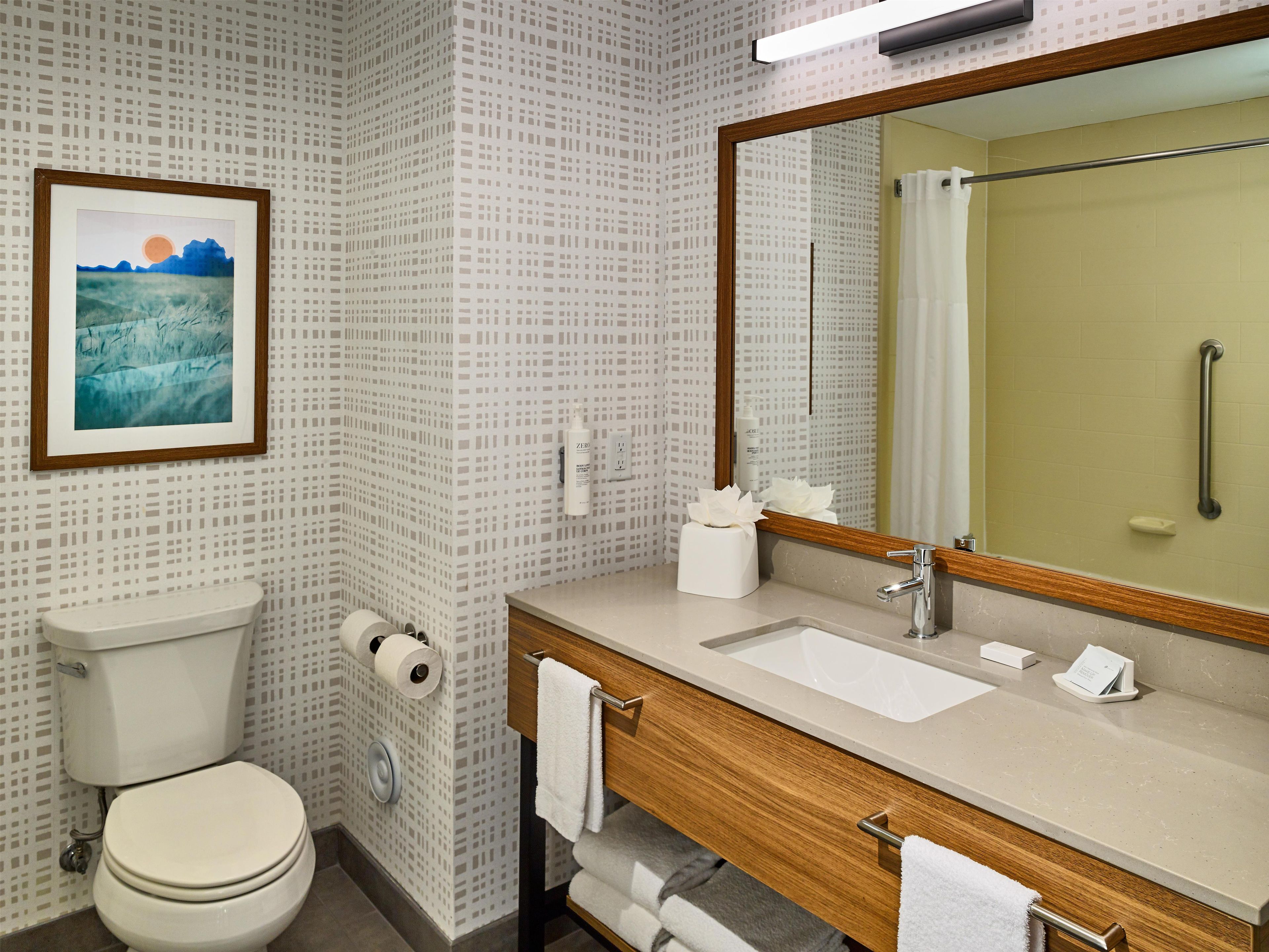 A bathroom with a toilet, sink, mirror, and a framed picture on the wall.