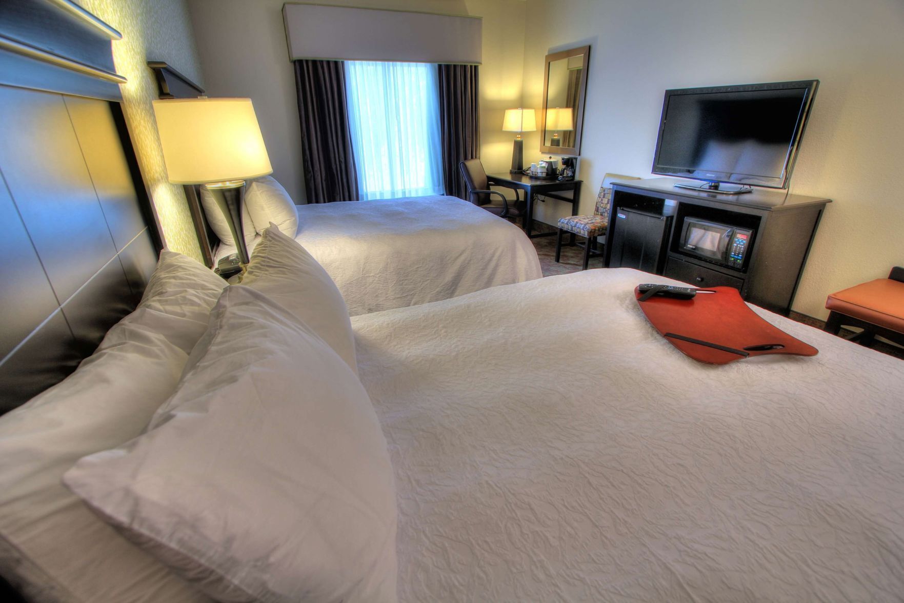 A hotel room with two beds, a desk with a chair, a television, and a microwave.