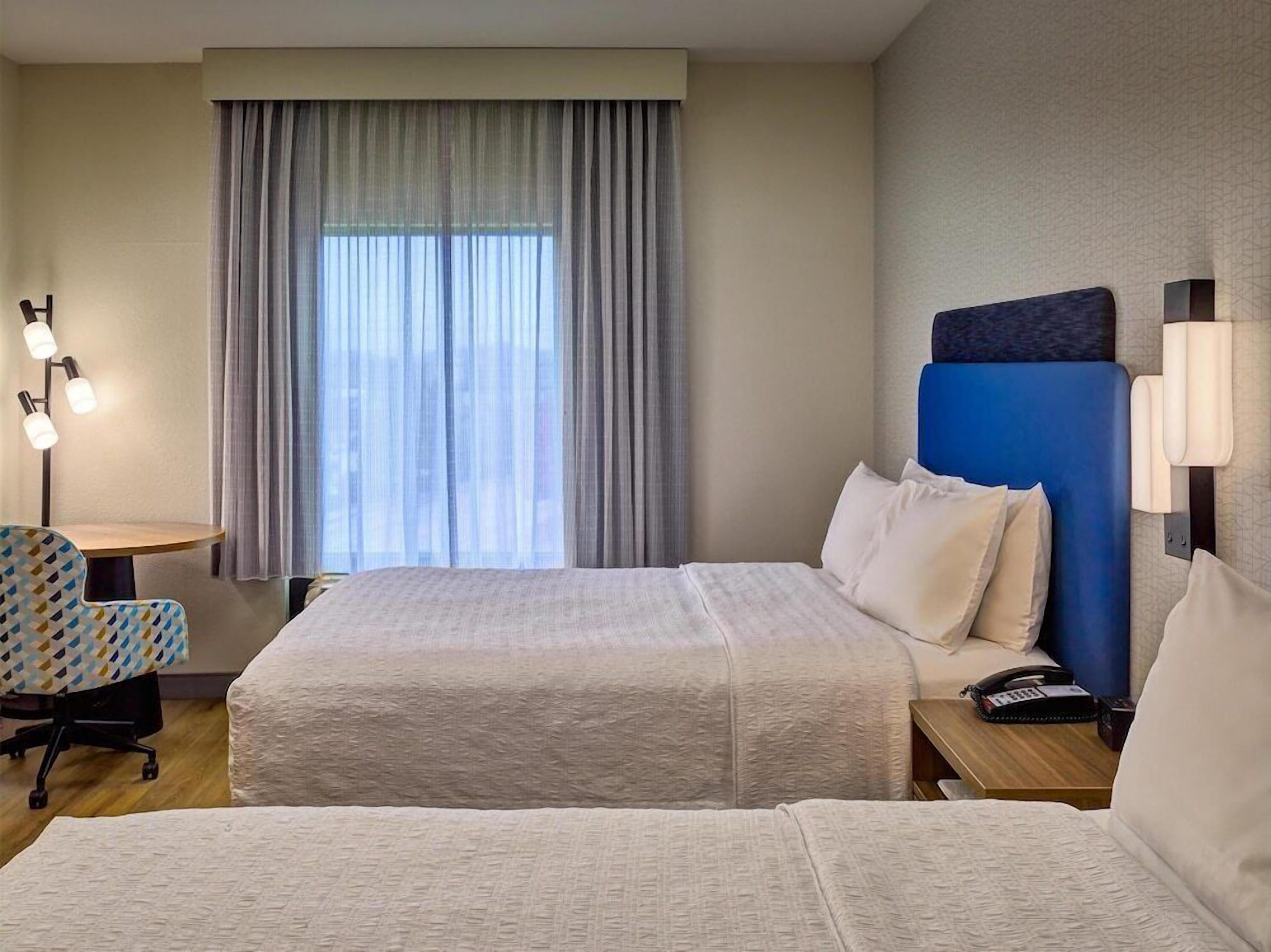 Een hotelkamer met twee bedden, een bureau, een stoel en een groot raam met gordijnen.