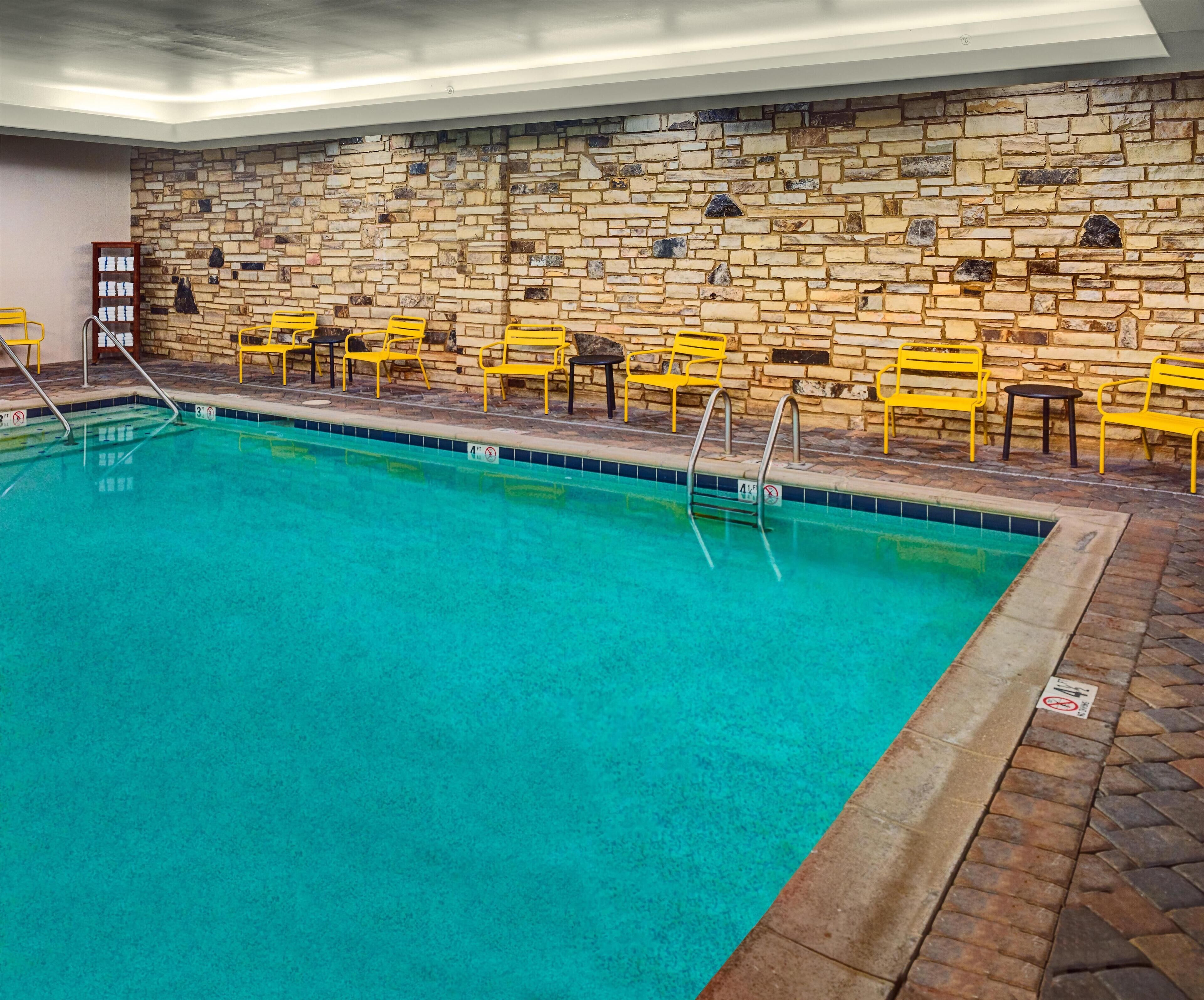 Una piscina interior amb un mur de pedra de fons i cadires grogues al voltant de la vora.