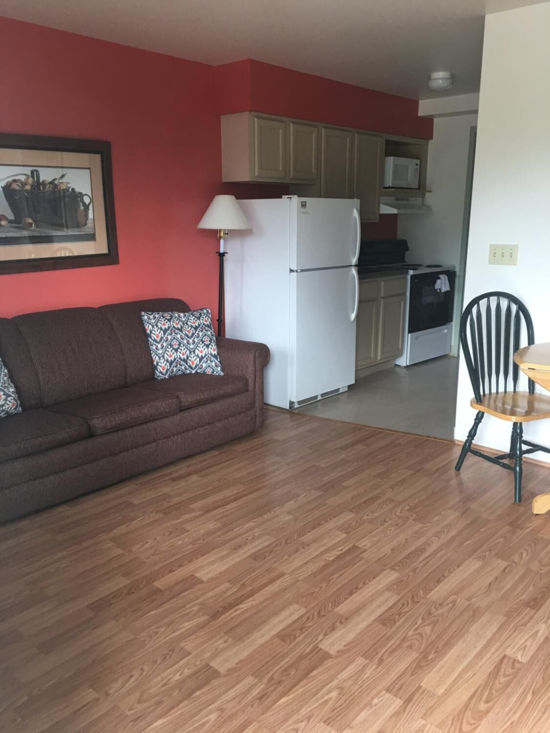 A compact living space with a brown sofa, a dining table with a chair, a white refrigerator, a microwave, and a stove.