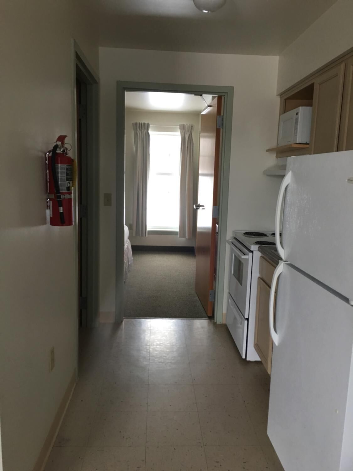 Un pasillo estrecho que conduce a una cocina con un refrigerador blanco, una estufa y un extintor de incendios en la pared.