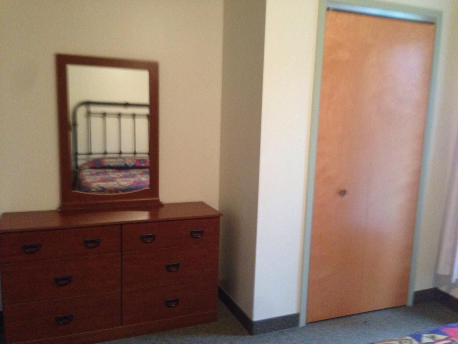 A room with a wooden dresser, a metal bed frame, and a wooden door.