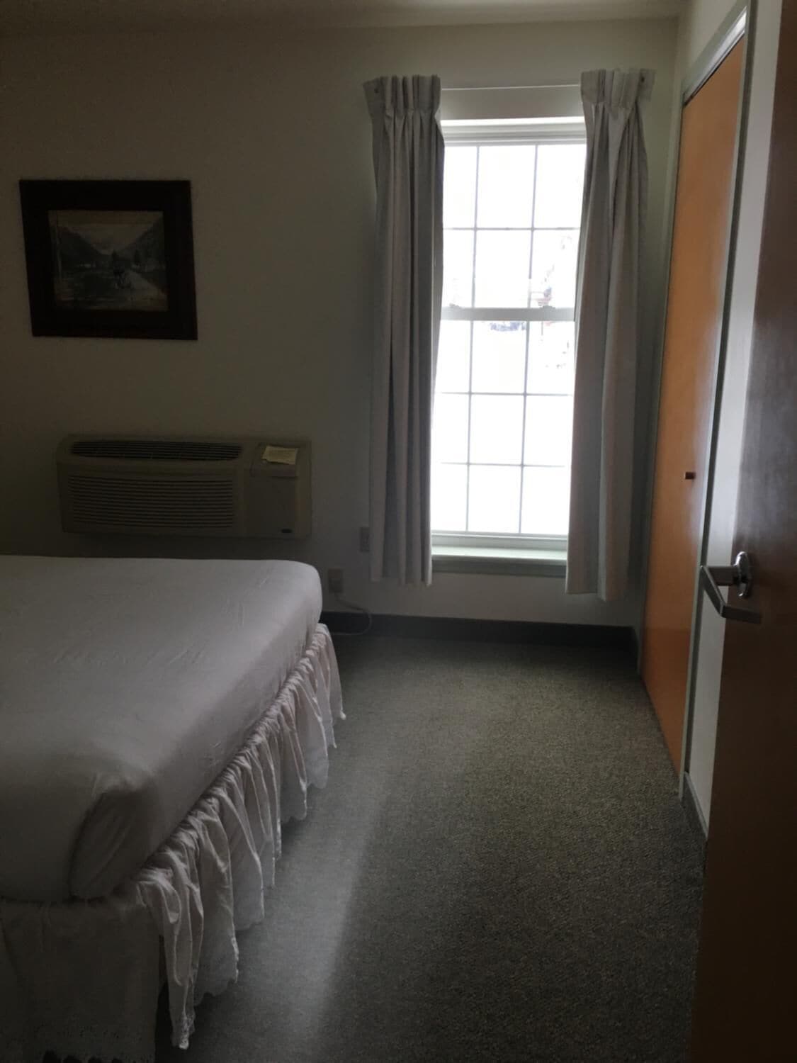 Una habitación de hotel con una cama, un ventanal con cortinas, un radiador y una puerta.