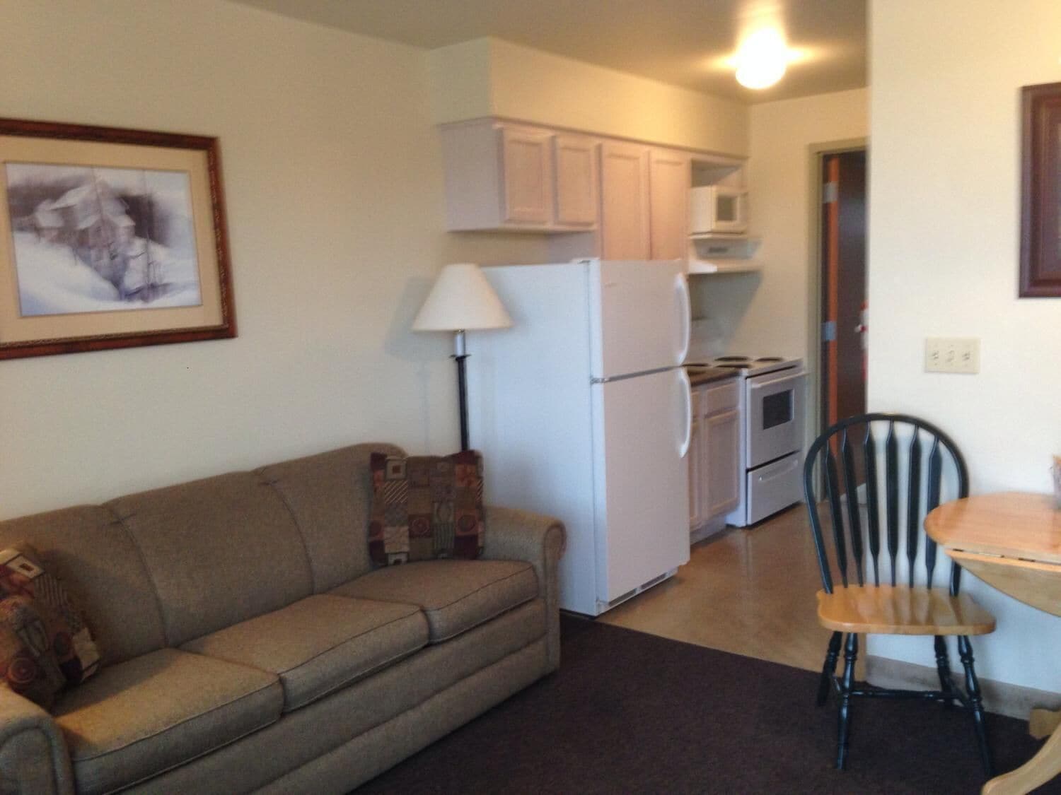 A compact living space with a sofa, a dining table, a chair, a refrigerator, a stove, and cabinets.