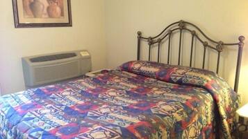A bed with a patterned bedspread, a wall-mounted air conditioner, and a framed picture above the bed.
