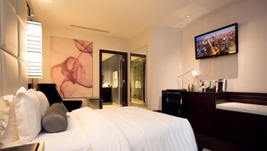 Camera d'albergo con un letto grande, una scrivania con una lampada, una TV e un bagno visibile attraverso una porta aperta.