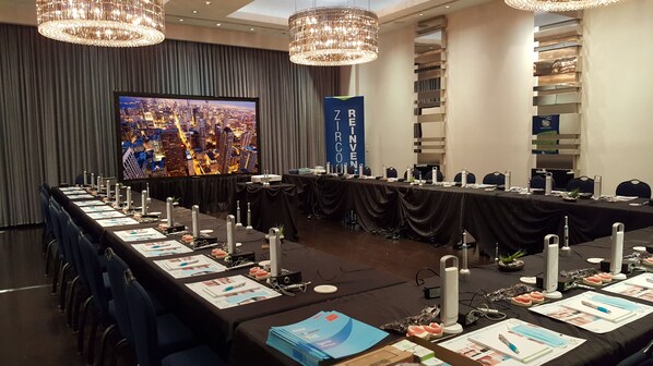 A conference room with a long table, chairs, a large screen, and a banner.