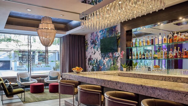 Zona bar moderna con bancone in marmo, sgabelli in pelle, un lampadario e una TV a parete.