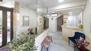 A hotel lobby with a reception desk, a bench, a chair, and a potted plant. - Faros Beach Hotel (Rethymno)