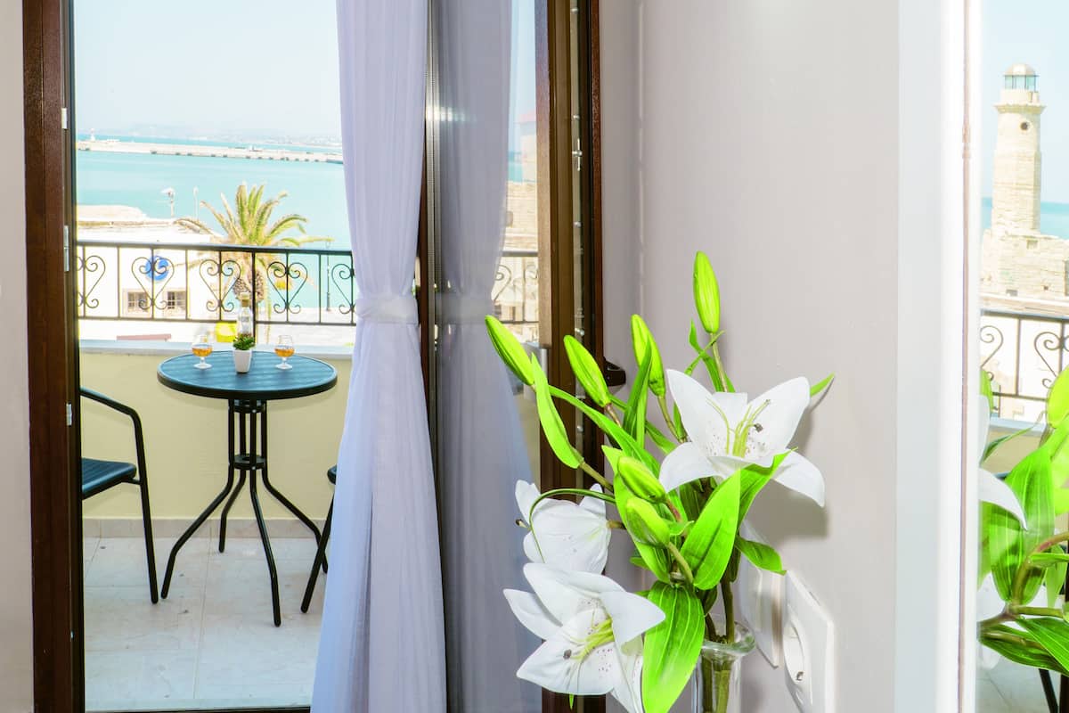 A balcony with a table and chairs, a vase with flowers, and a view of the sea and a lighthouse.