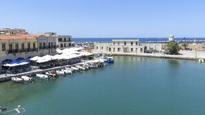 A marina with boats docked, a waterfront restaurant, and buildings in the background. - Faros Beach Hotel (Rethymno)