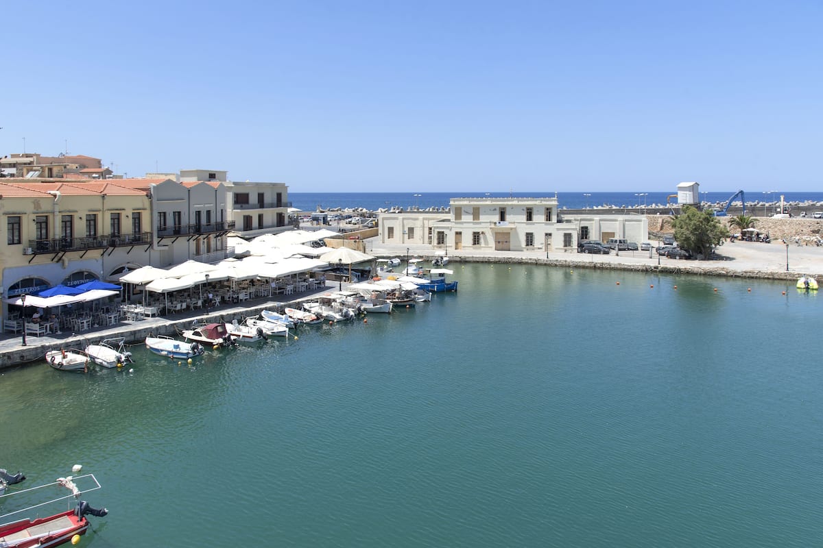 A marina with boats docked, a waterfront restaurant, and buildings in the background.