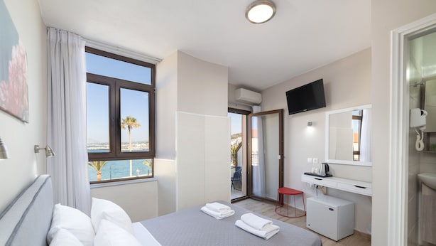 A hotel room with a bed, a desk, a TV, and a view of the sea. - Faros Beach Hotel (Rethymno)